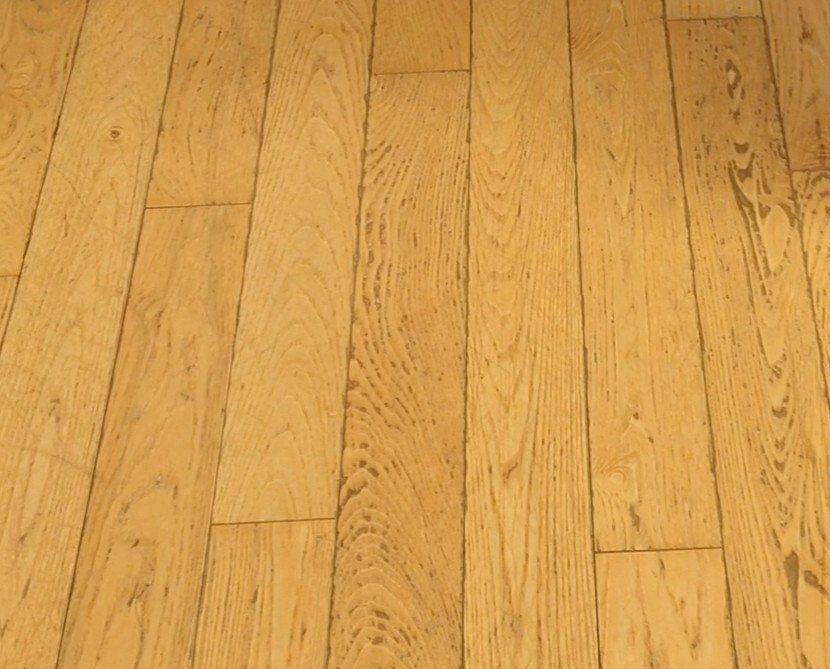 Wooden floorboards, light brown and textured, fill the frame at a diagonal angle.