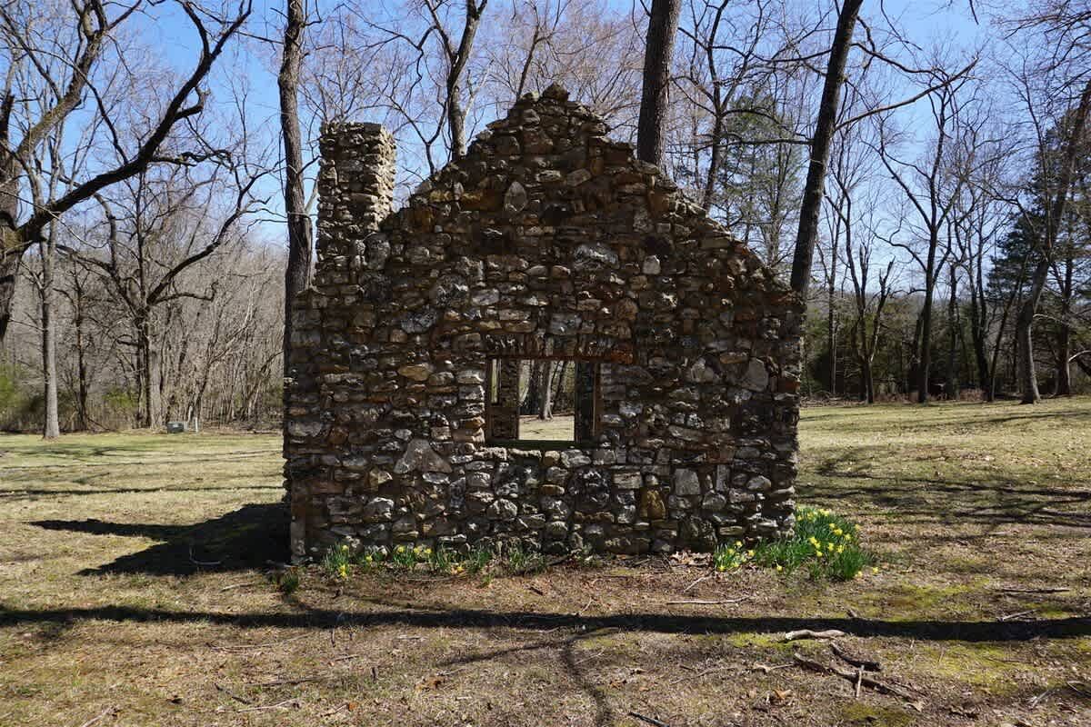 An old stone house in the middle of a field with trees in the background.