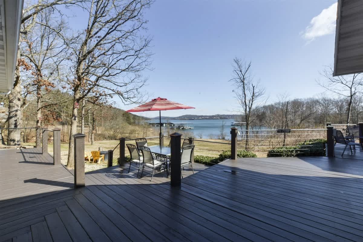 A large deck with a table and chairs and an umbrella overlooking a lake.