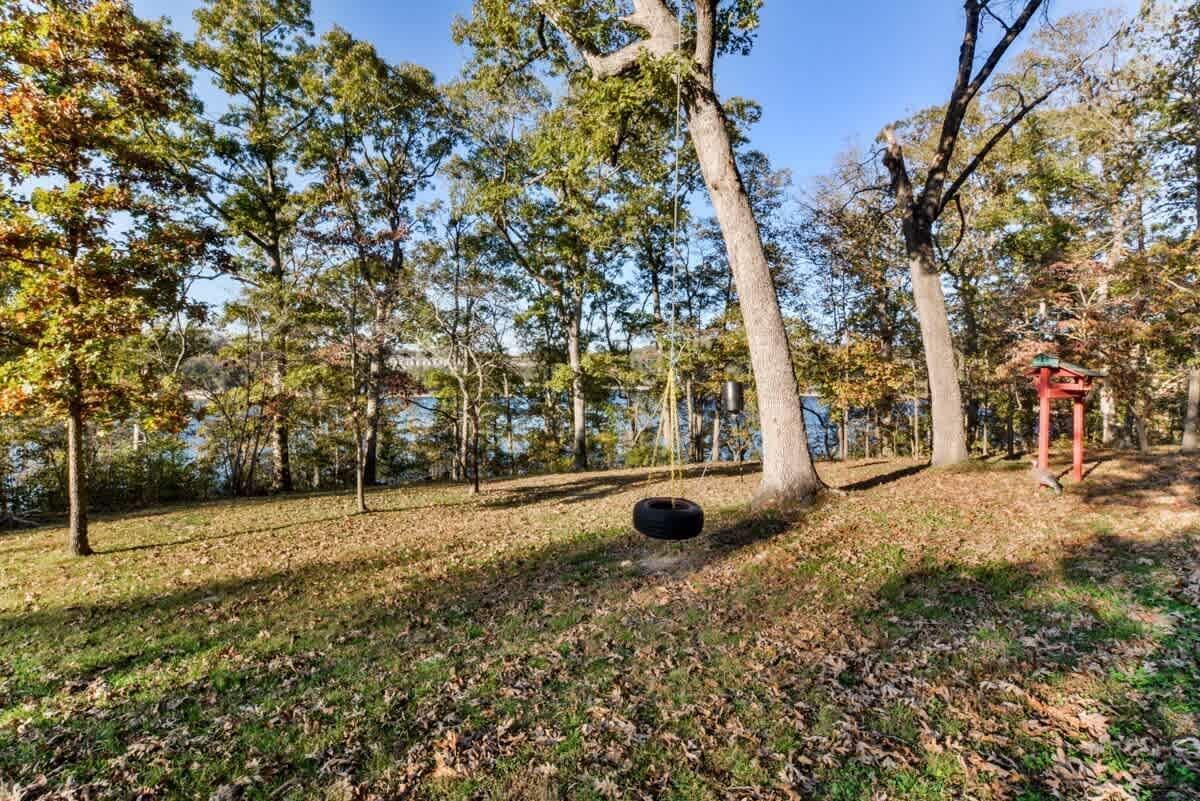 A tire swing is sitting in the middle of a field surrounded by trees.