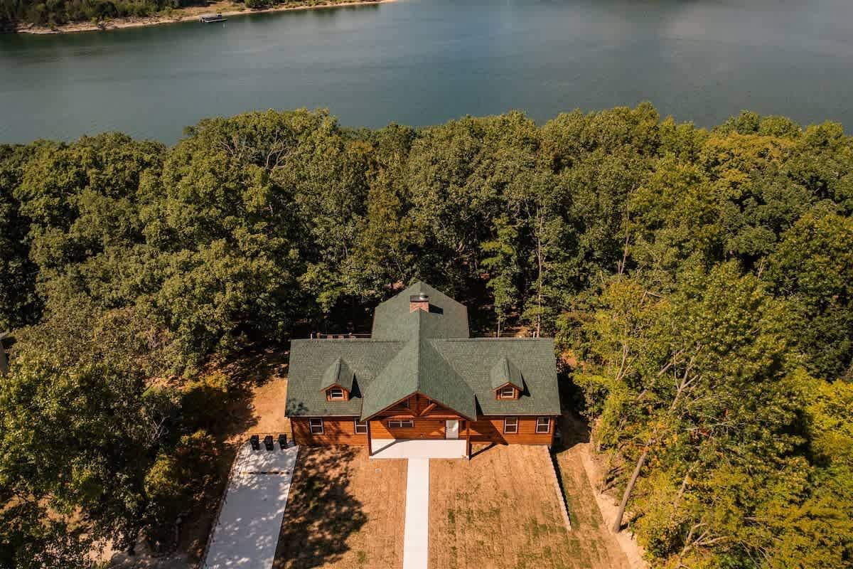 An aerial view of a log cabin surrounded by trees next to a lake.