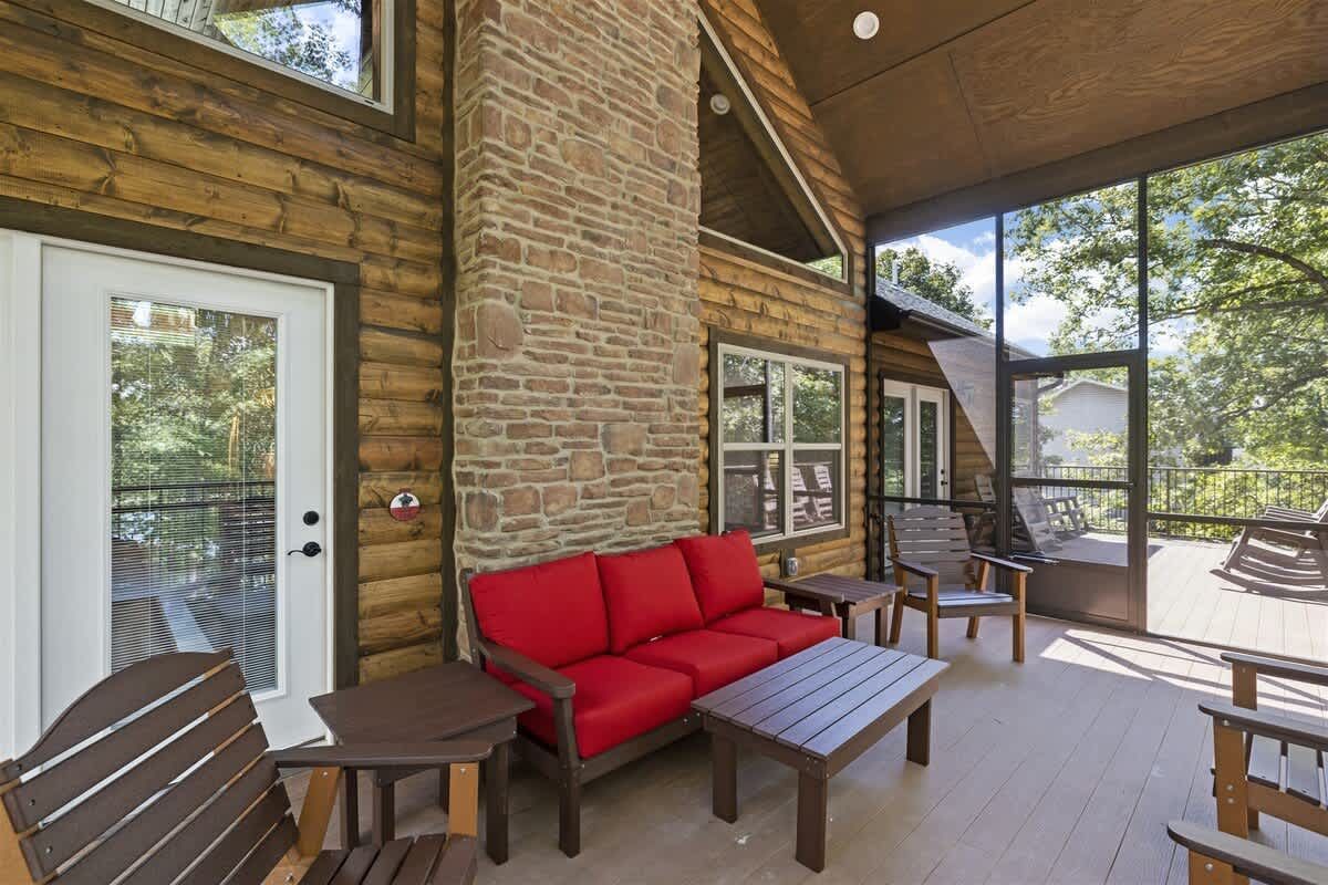 A screened in porch with a couch , chairs , tables and a fireplace.
