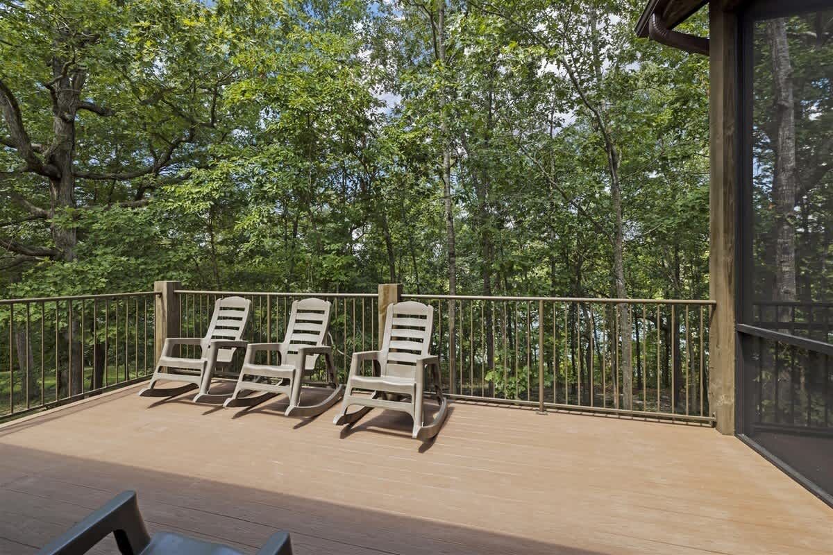 A deck with a railing and chairs on it with trees in the background.