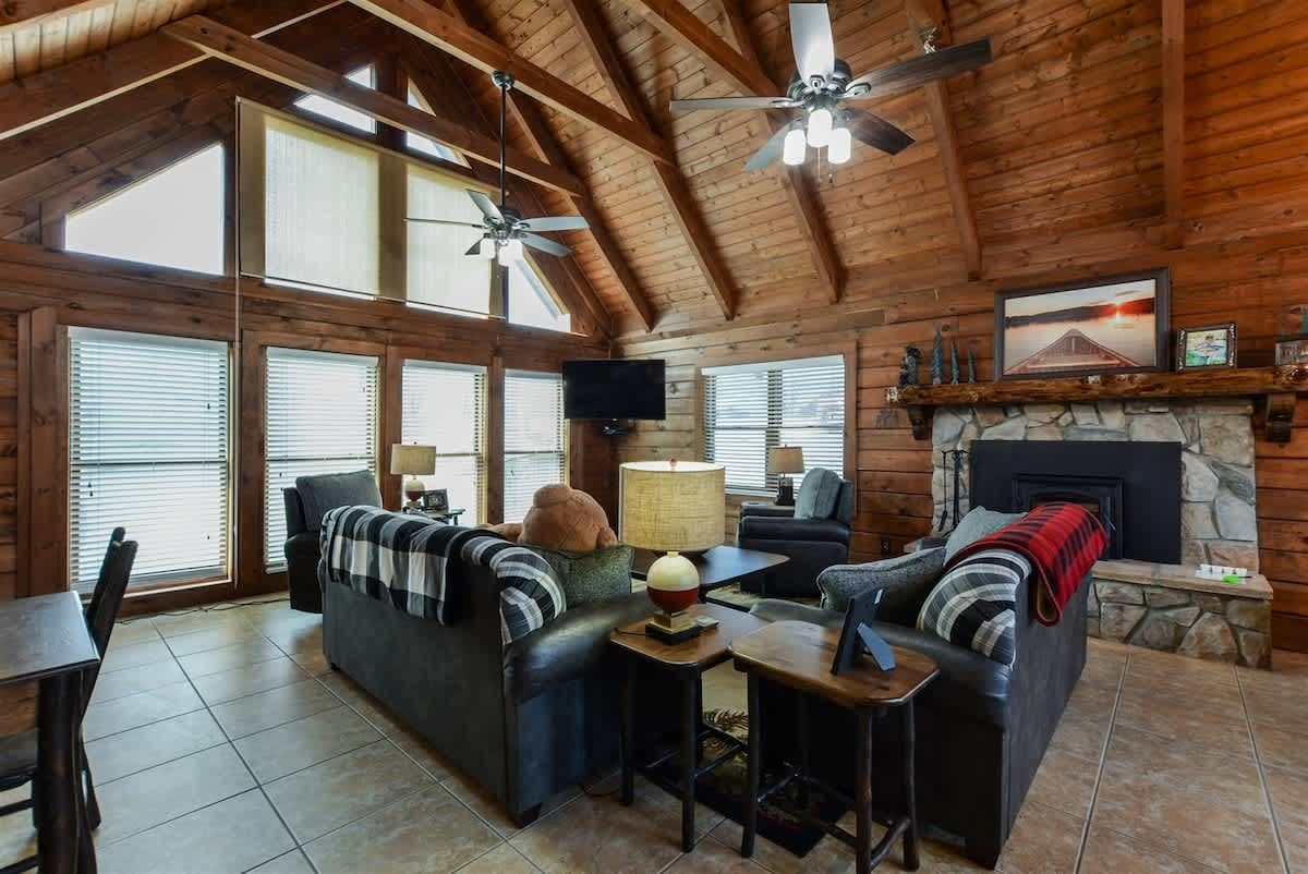 A living room in a log cabin with a couch , fireplace , television and ceiling fan.