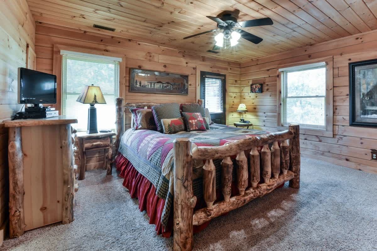 A bedroom in a log cabin with a wooden bed and a ceiling fan.