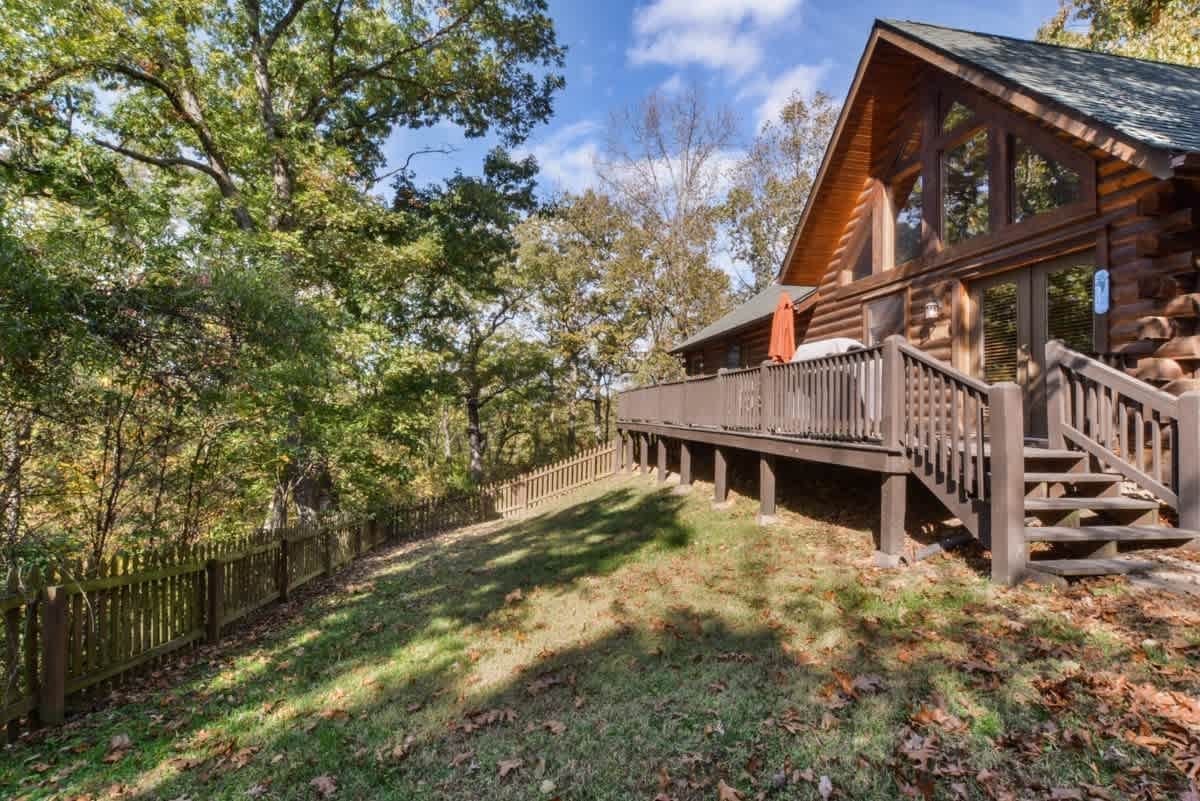 A large log cabin with a large deck in the middle of a forest.
