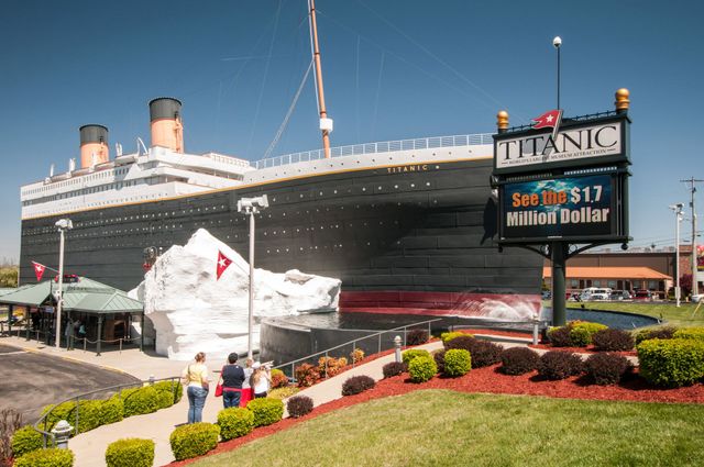 A group of people are walking in front of a replica of the titanic ship.
