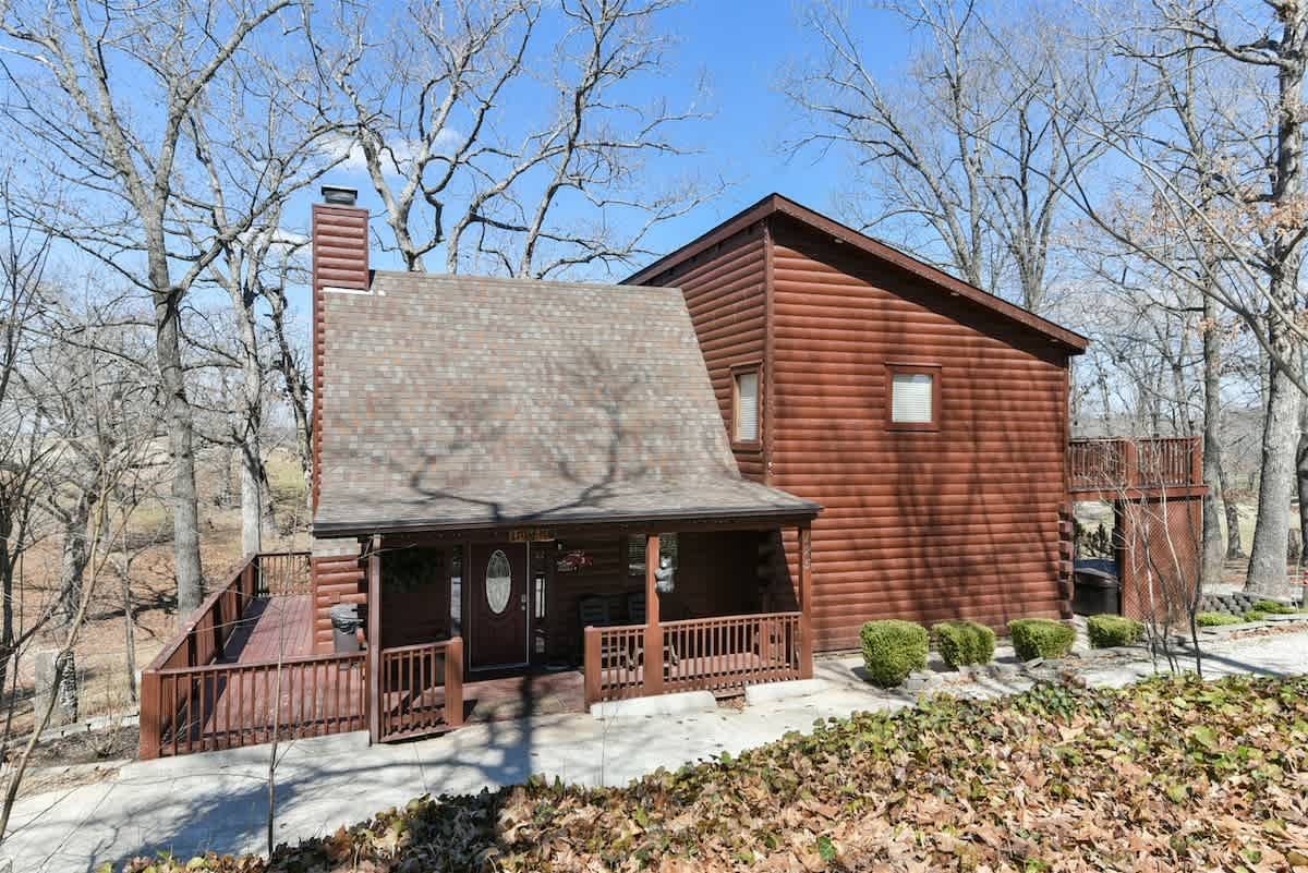 A large log cabin with a porch and a deck in the middle of a forest.
