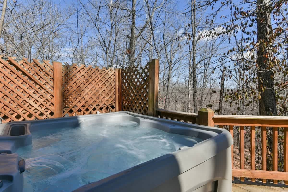 A hot tub is sitting on a deck next to a wooden fence.