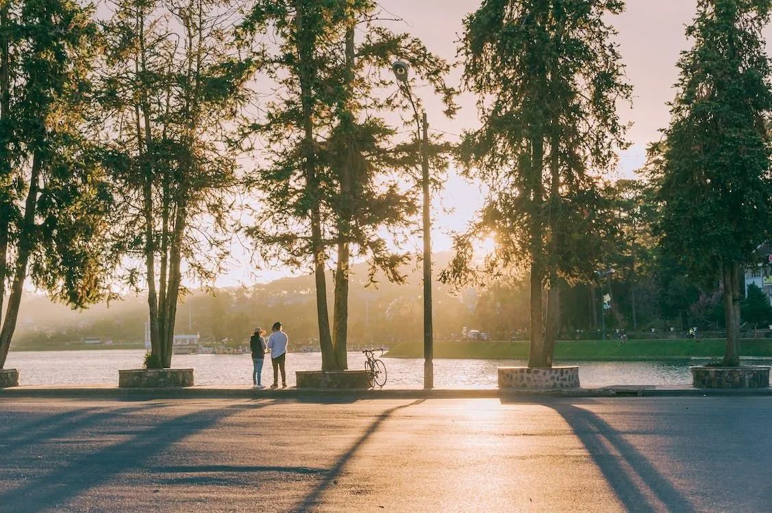 A couple of people standing next to a lake at sunset.