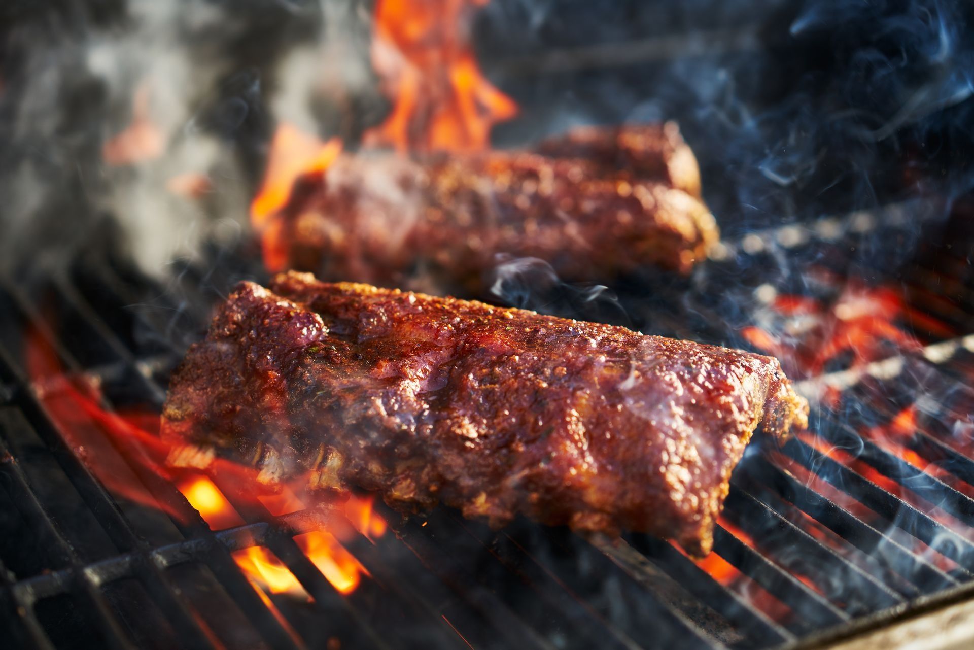 Two ribs are cooking on a grill with flames.