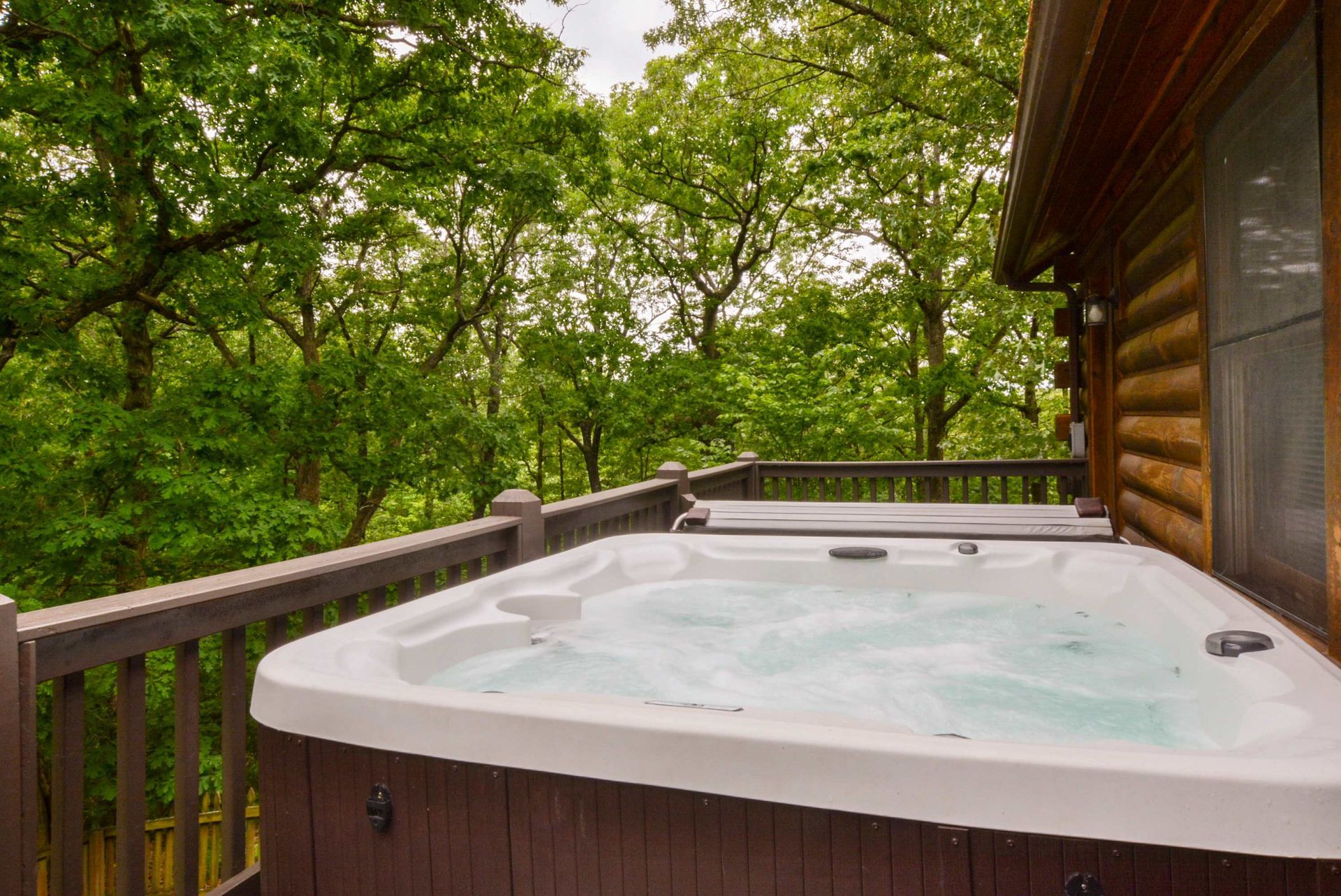 A hot tub is on the deck of a log cabin.