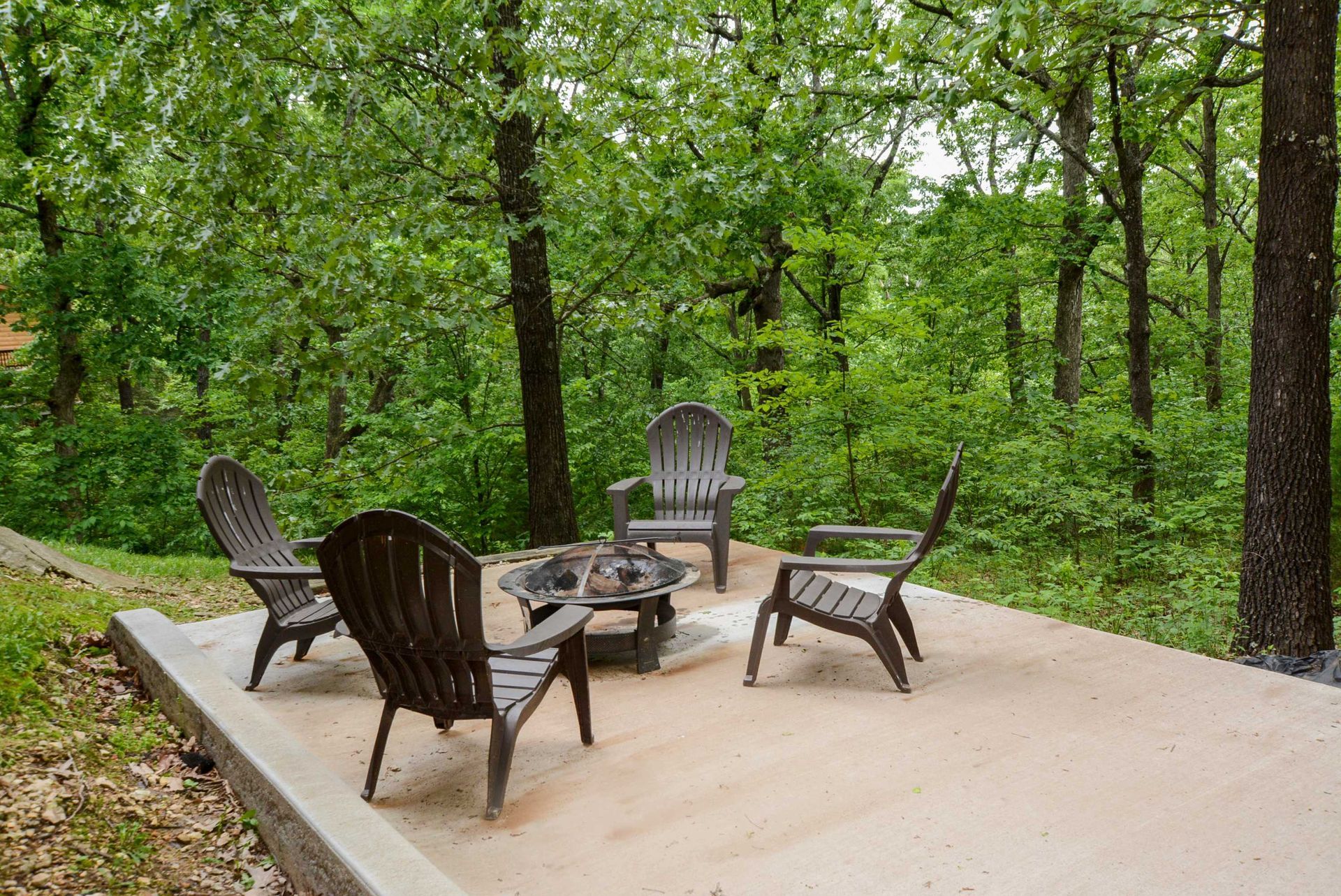 A group of chairs are sitting around a fire pit in the middle of a forest.