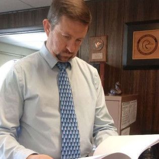 A man in a shirt and tie is reading a book.