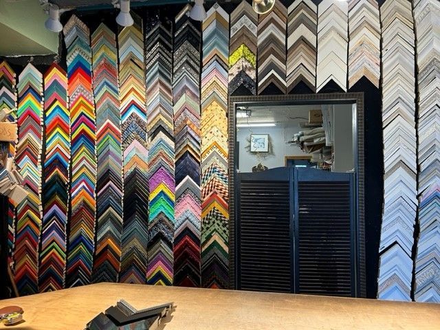 Colorful chevron-patterned frame samples wall with a black doorway opening in a shop interior