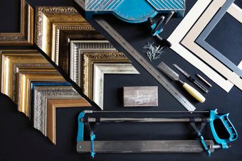 Assorted picture frames, saws, and tools arranged on a dark surface for framing work