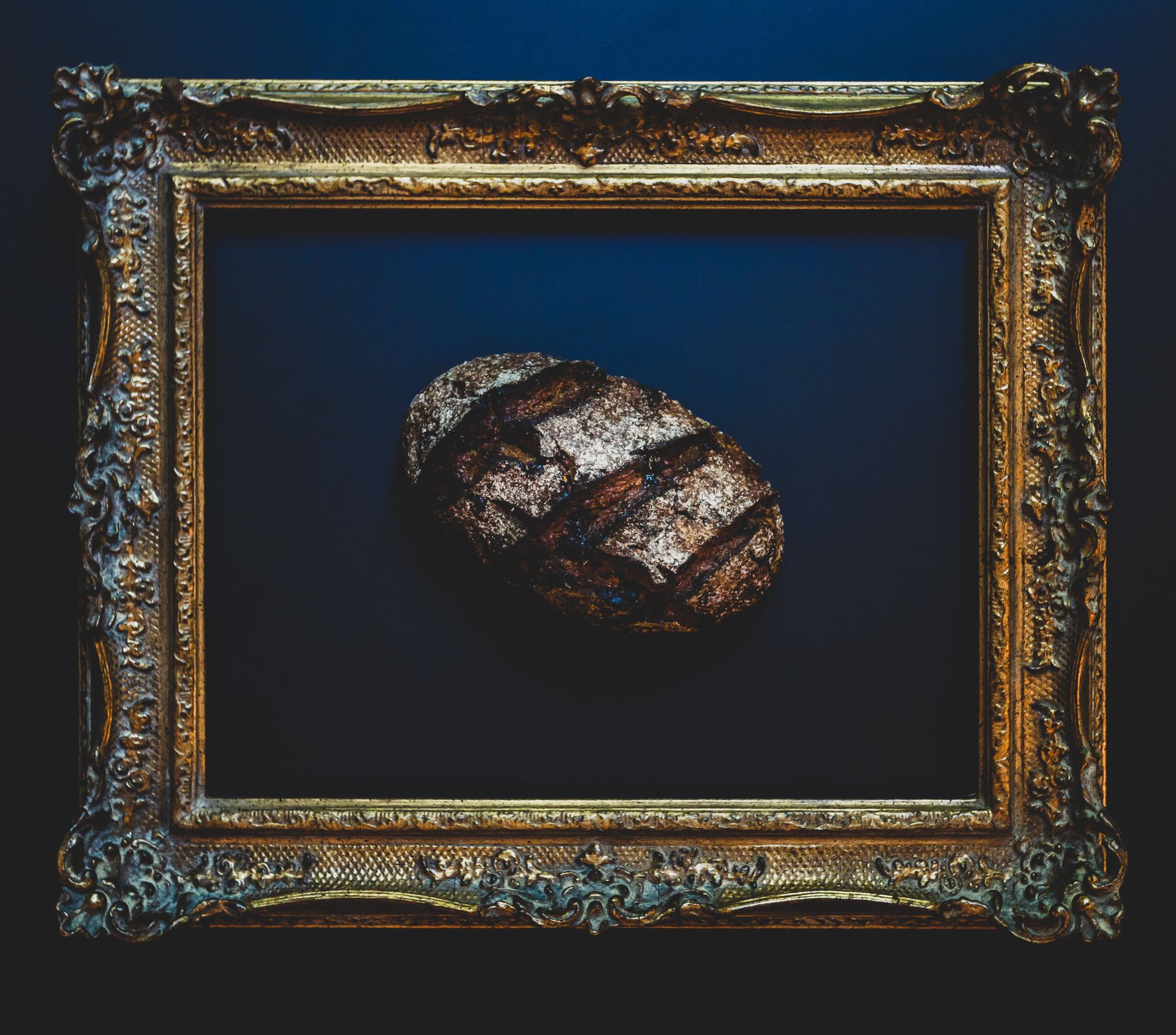Ornate gold frame around a dark blue background with a small textured oval object in the center