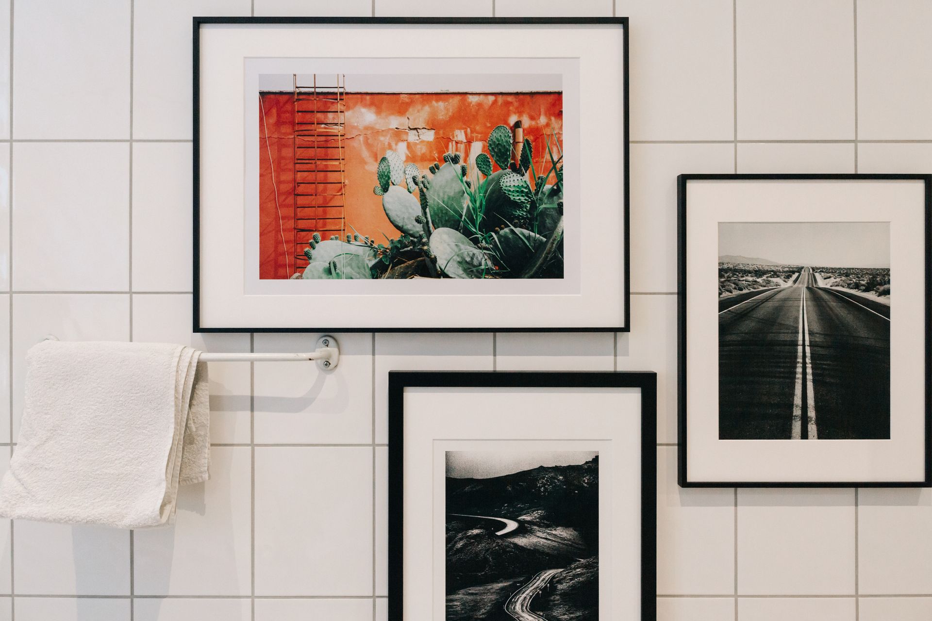 Framed art prints on a tiled wall above a white towel rack