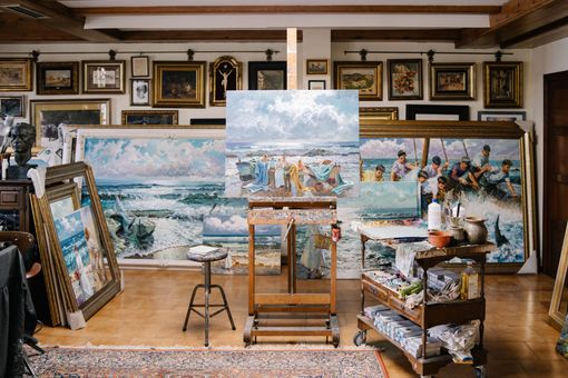 Art studio with multiple seascape paintings on easels and walls, including a large central canvas.