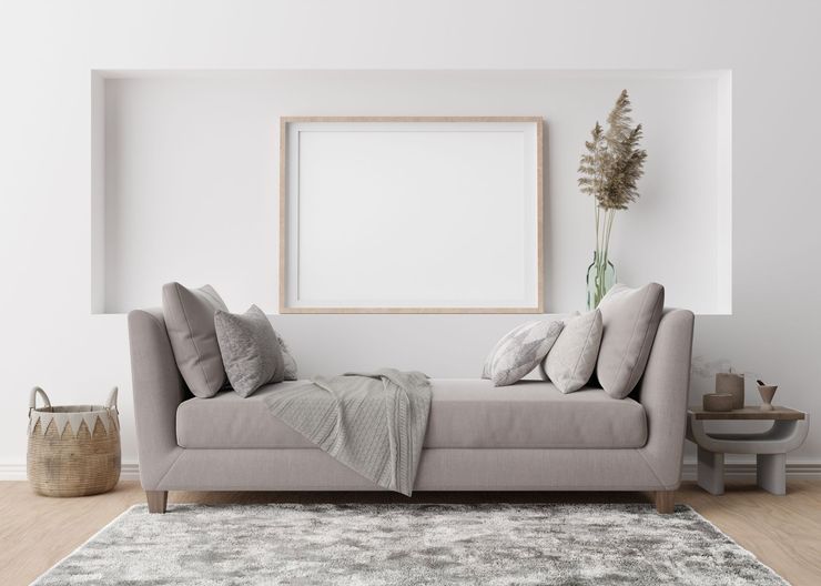 Minimalist living room with a beige sofa, framed wall art, and neutral decor on a textured rug.