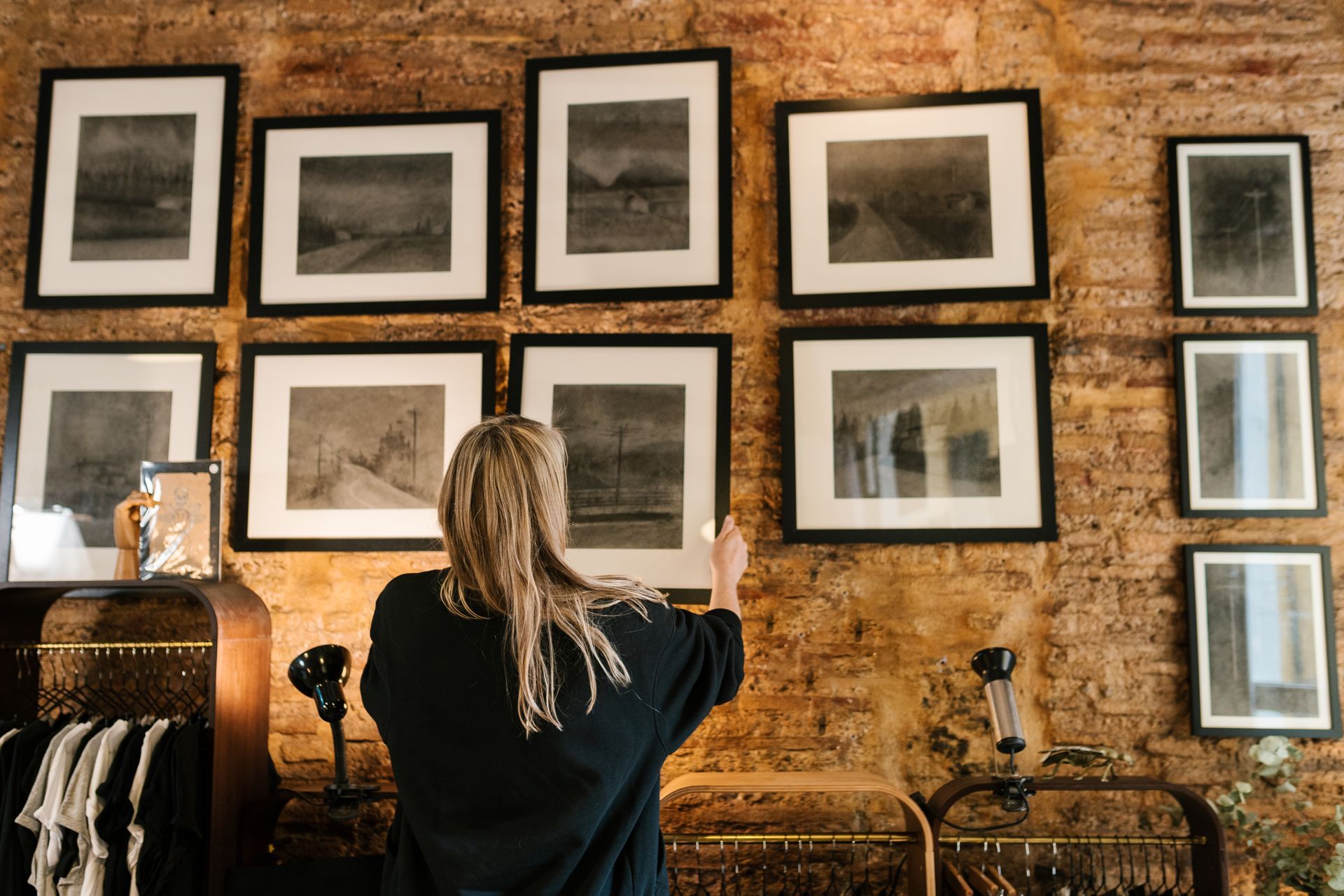 Person hanging framed photos on a brick gallery wall with black-and-white artwork.