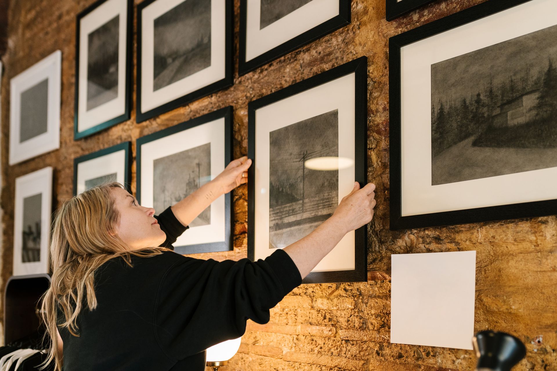 Person hanging framed artwork on a gallery wall of black-and-white photos