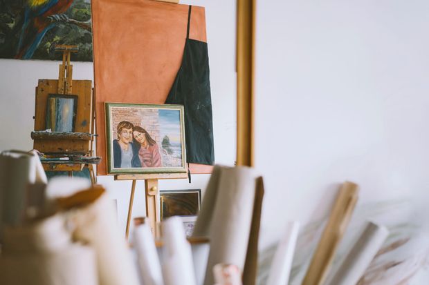 Framed portrait on an easel in a studio, with brushes and canvases in the foreground