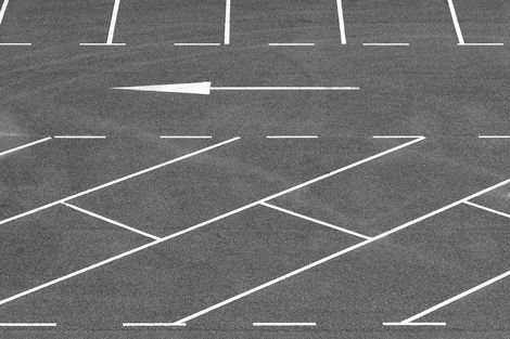 gray parking lot with diagonal car parking stripes, some horizontal parking stripes, and an arrow pointing to the left