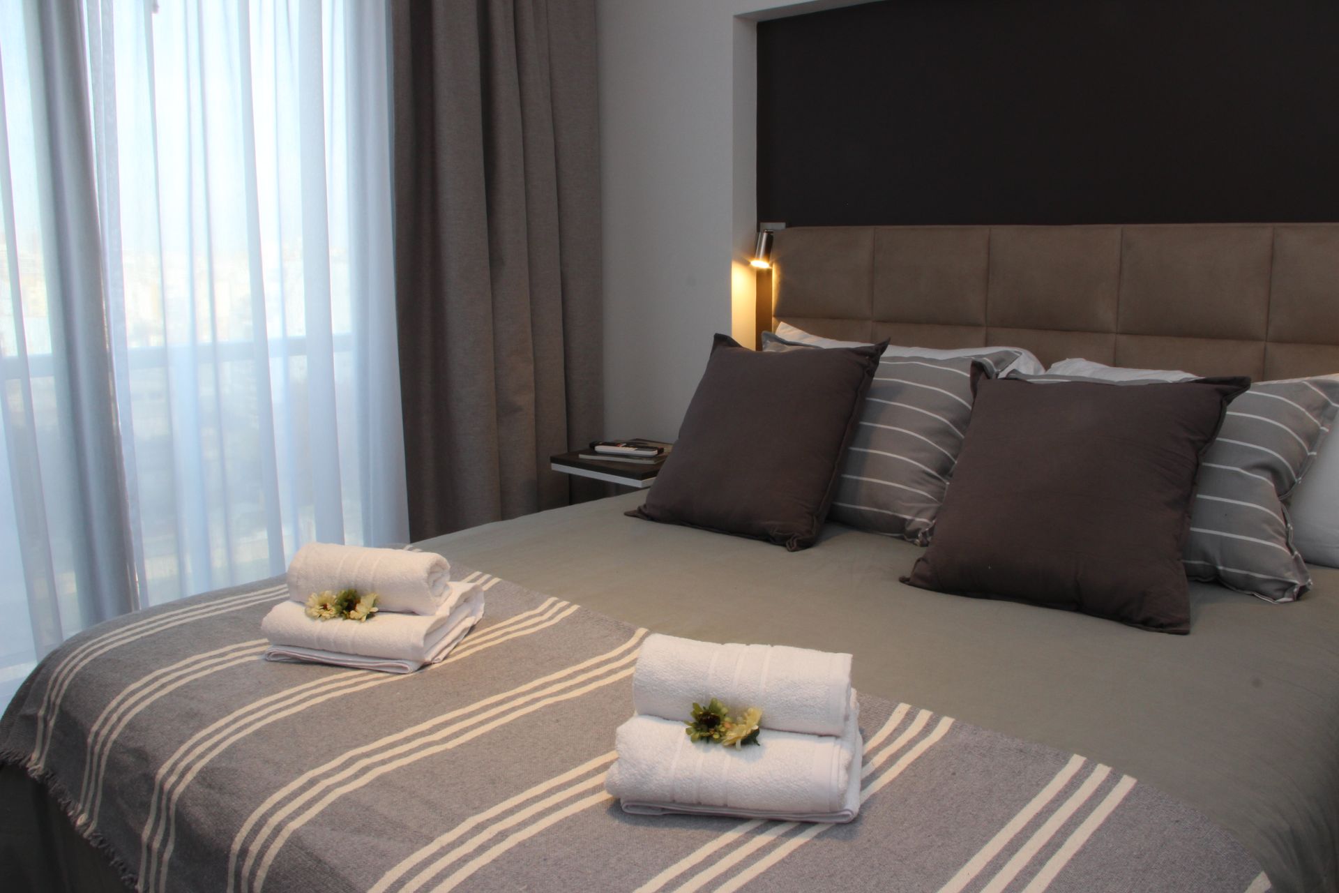 Un dormitorio con una cama, almohadas, toallas y una ventana.