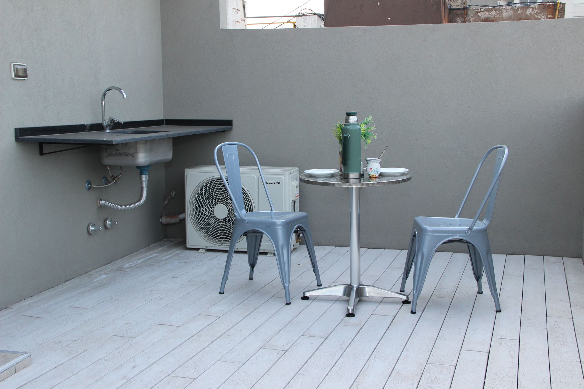 Una mesa y sillas en una terraza junto a un fregadero.