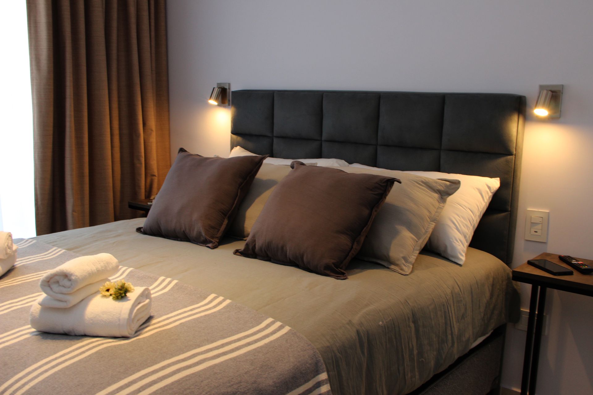 Una cama con una manta gris y almohadas marrones en un dormitorio.