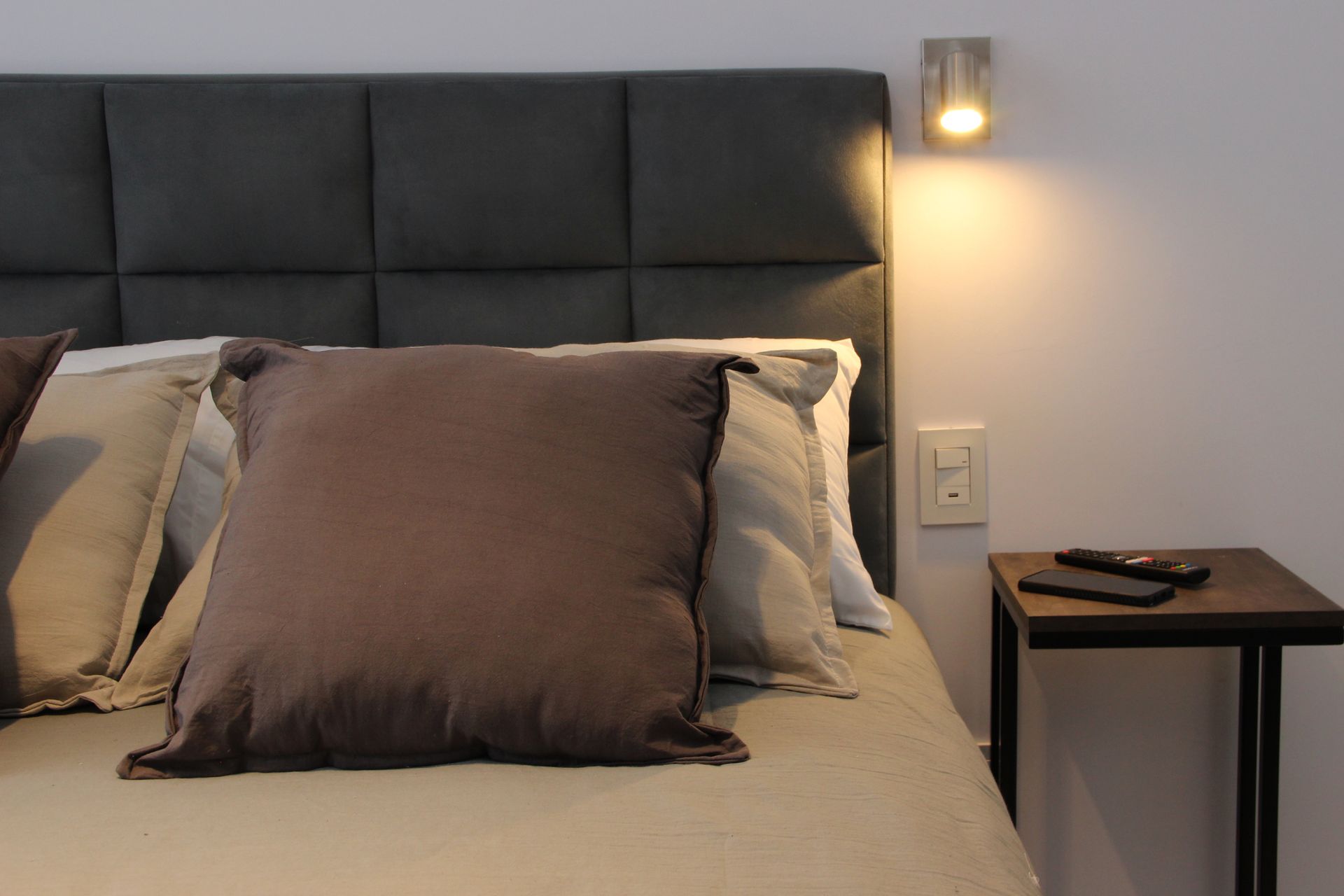 Una cama con cabecera gris y almohadas marrones.