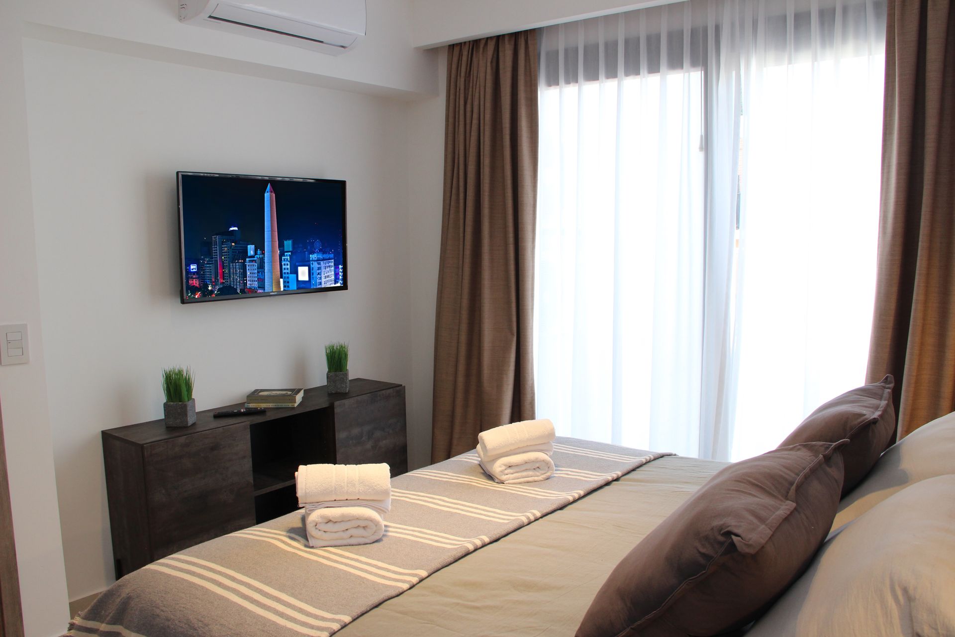 Un dormitorio con una cama grande y un televisor de pantalla plana en la pared.