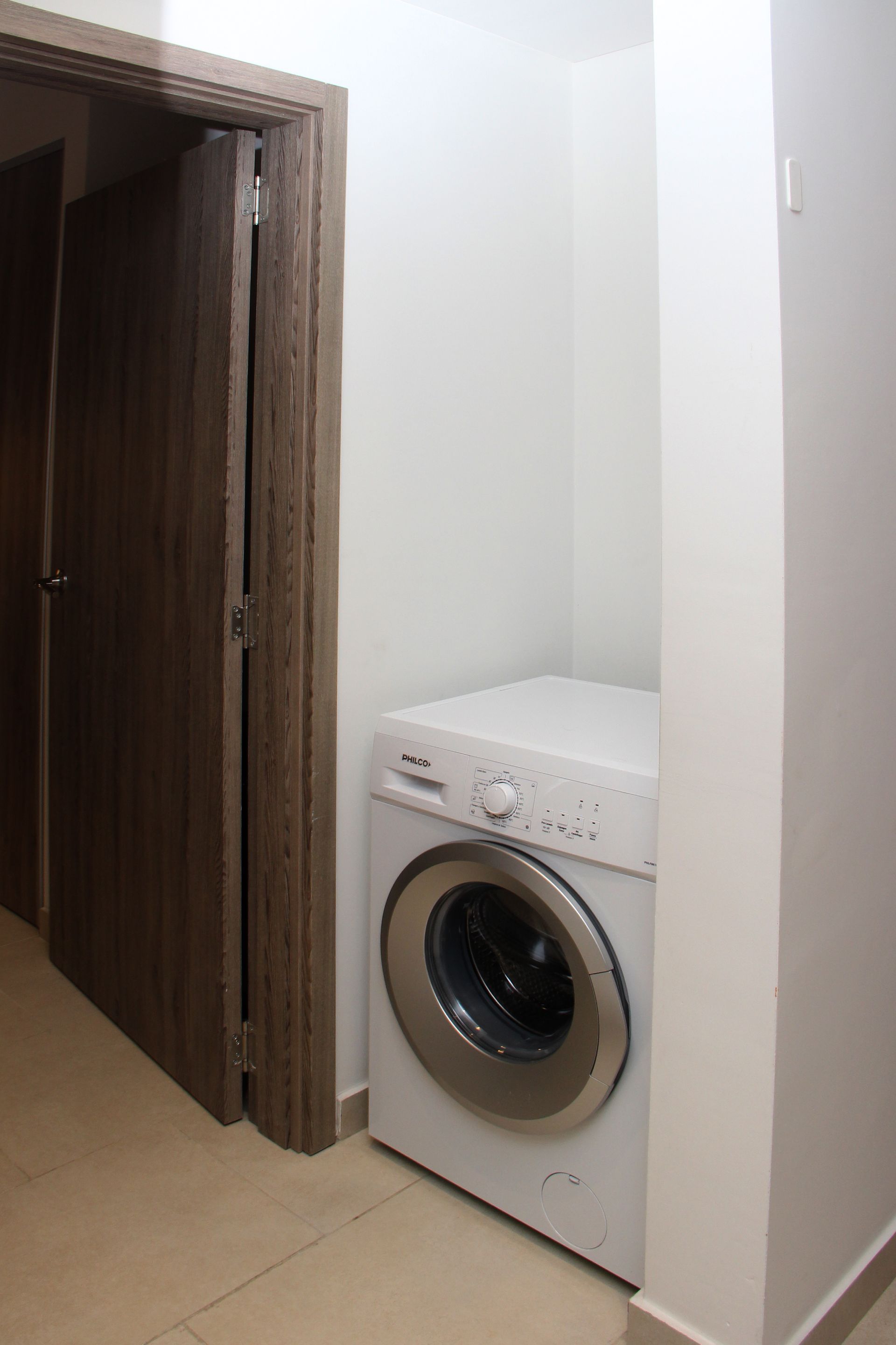 Una lavadora está en un rincón de una habitación, al lado de una puerta.