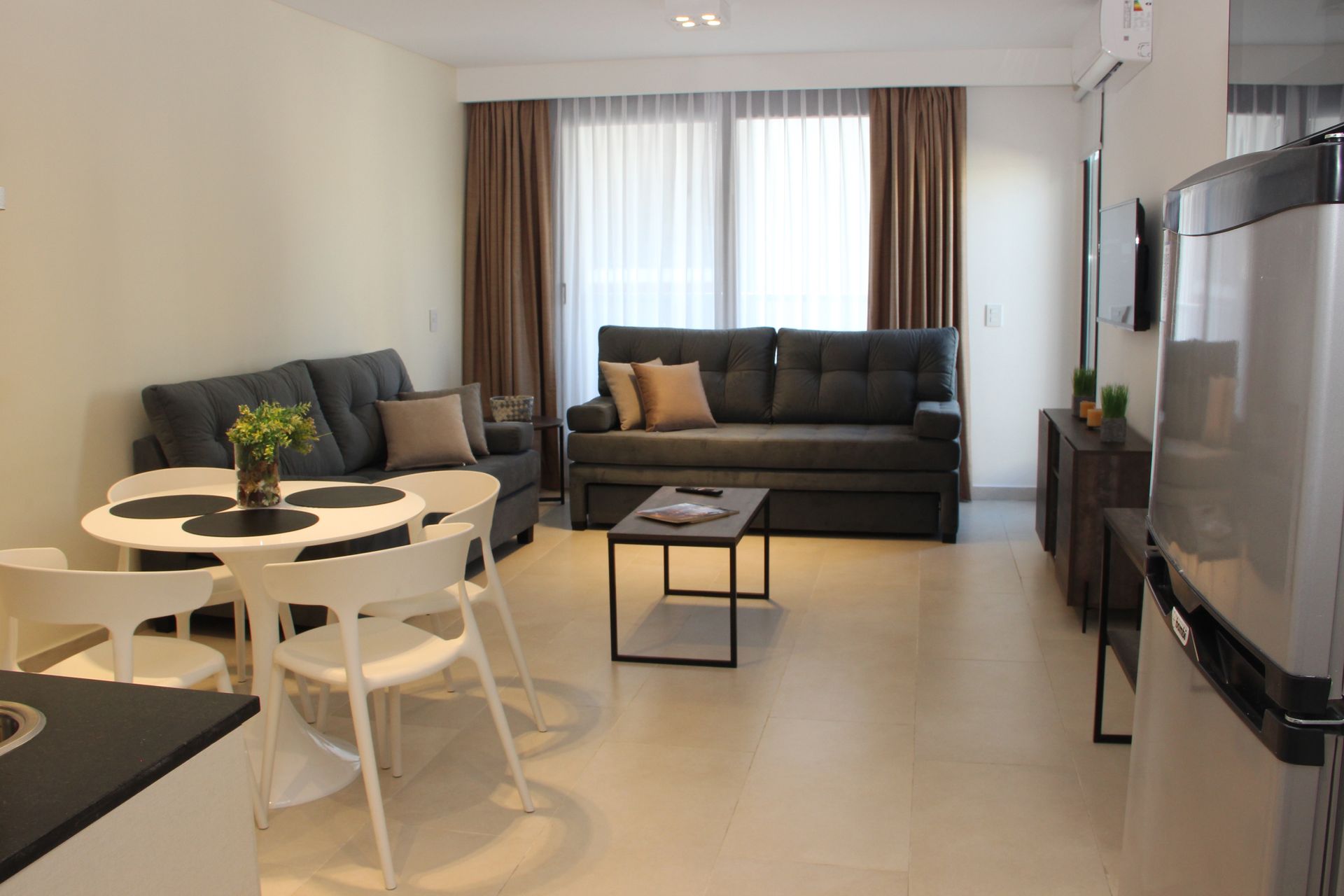 Una sala de estar con un sofá, una mesa, sillas y un refrigerador.