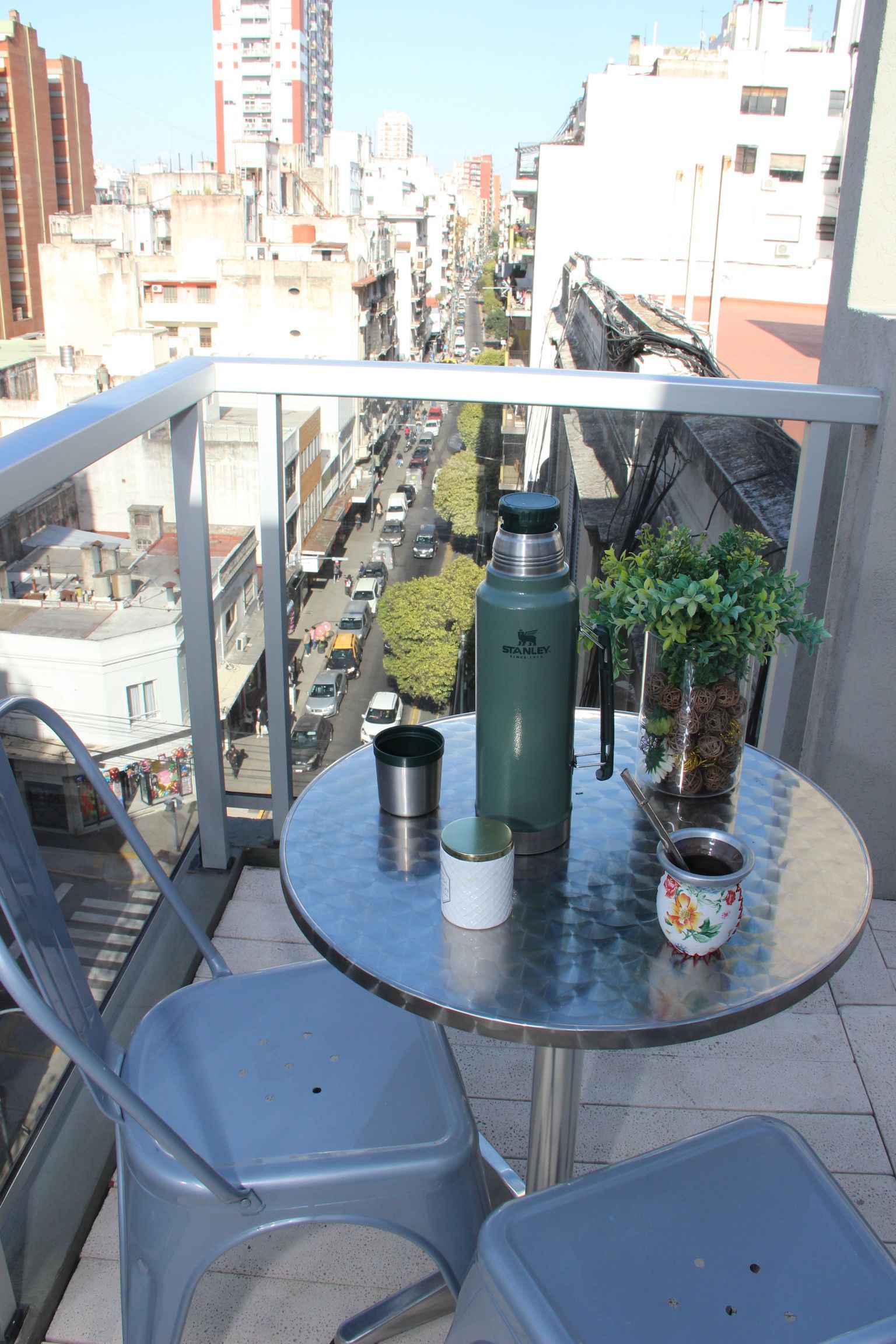 Una pequeña mesa y sillas en un balcón con vista a una ciudad.