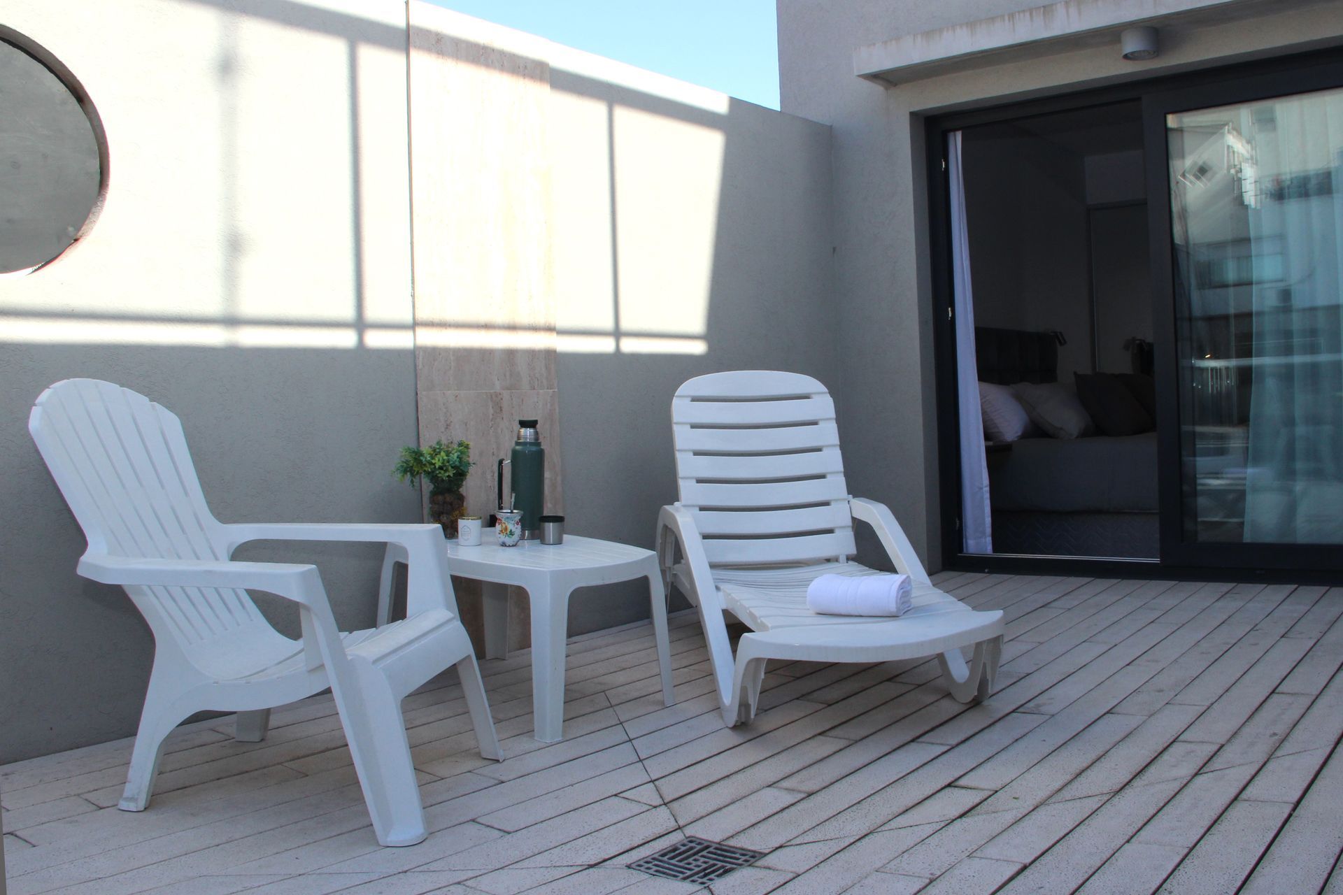 Dos sillas blancas están sentadas en una terraza de madera al lado de una mesa.