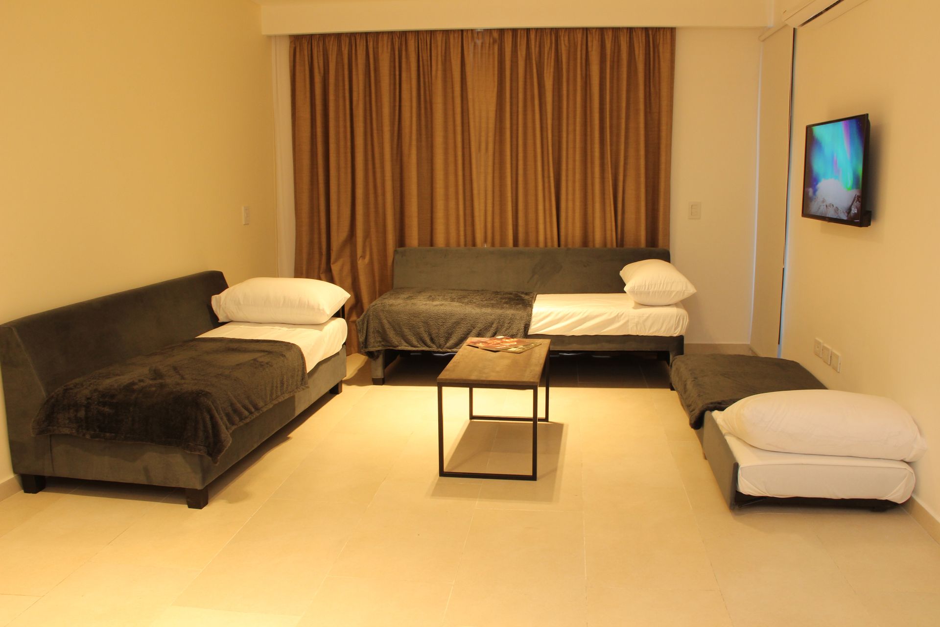 Una sala de estar con un sofá, dos camas, una mesa y un televisor.