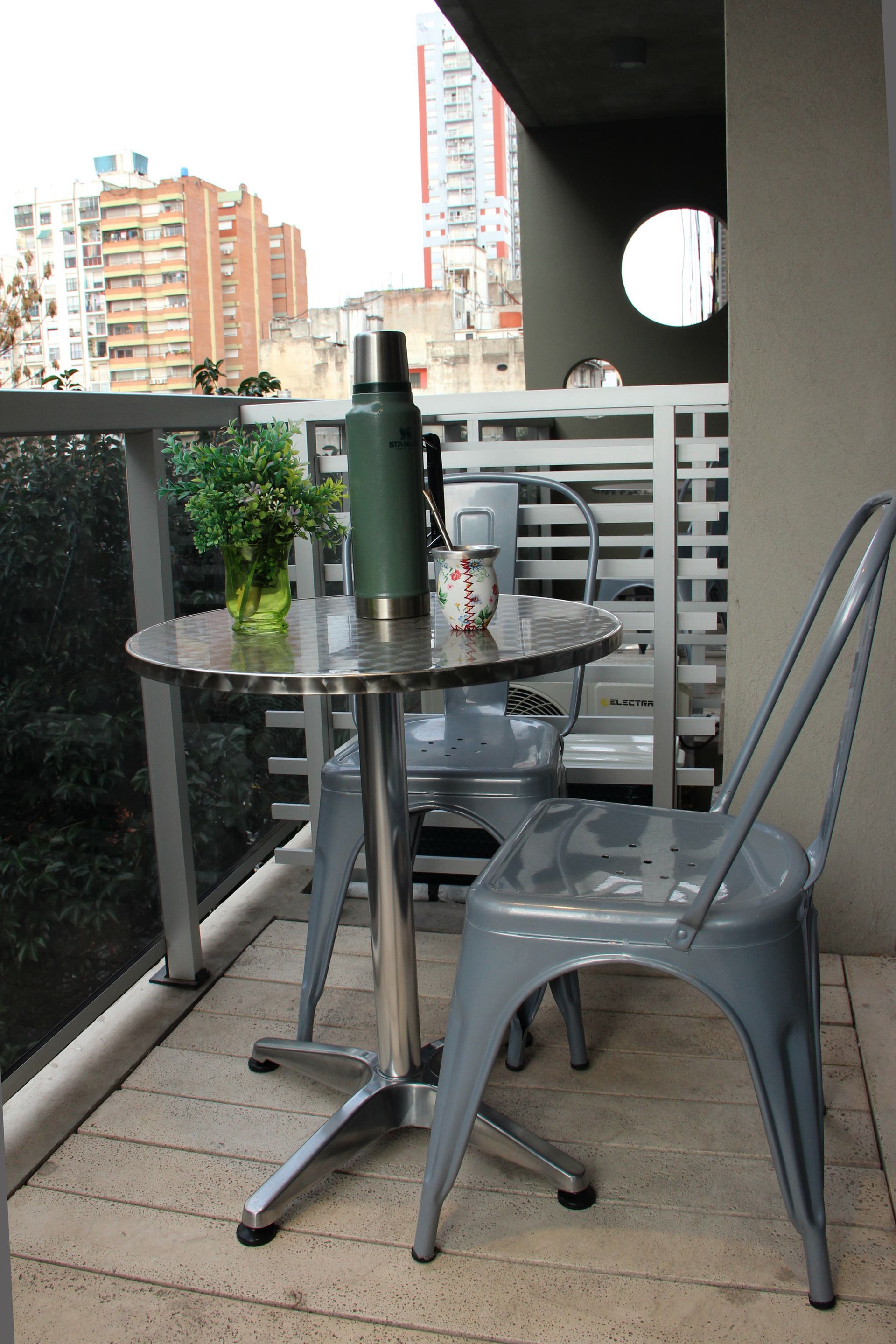 Un balcón con una mesa y sillas y un termo encima.