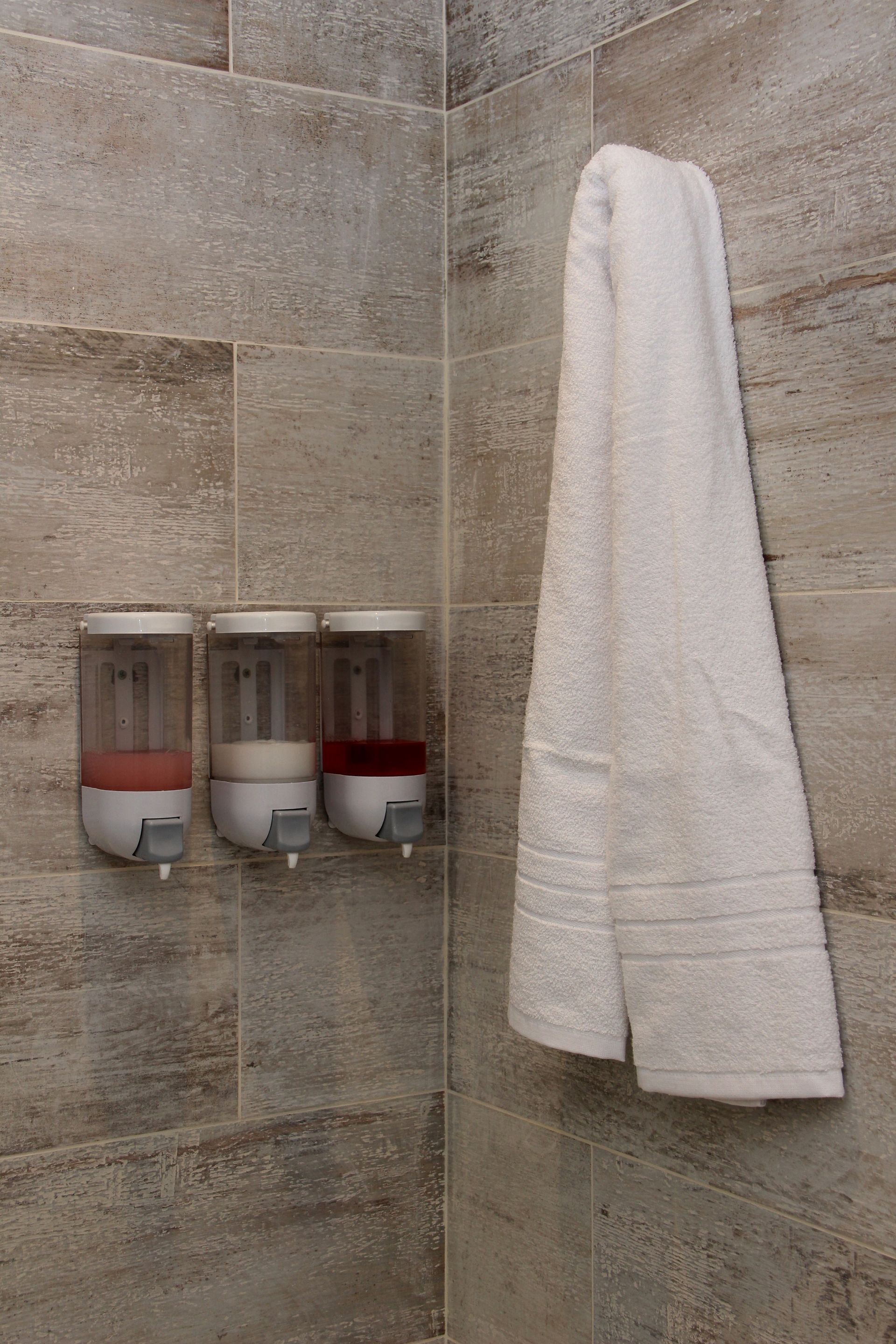 Una toalla está colgada en una ducha al lado de dispensadores de jabón.