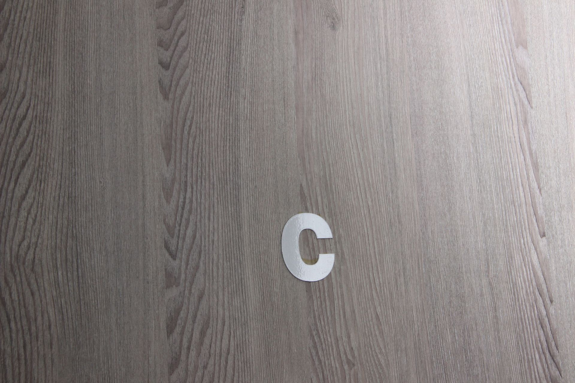 Una letra c blanca está sobre un piso de madera.