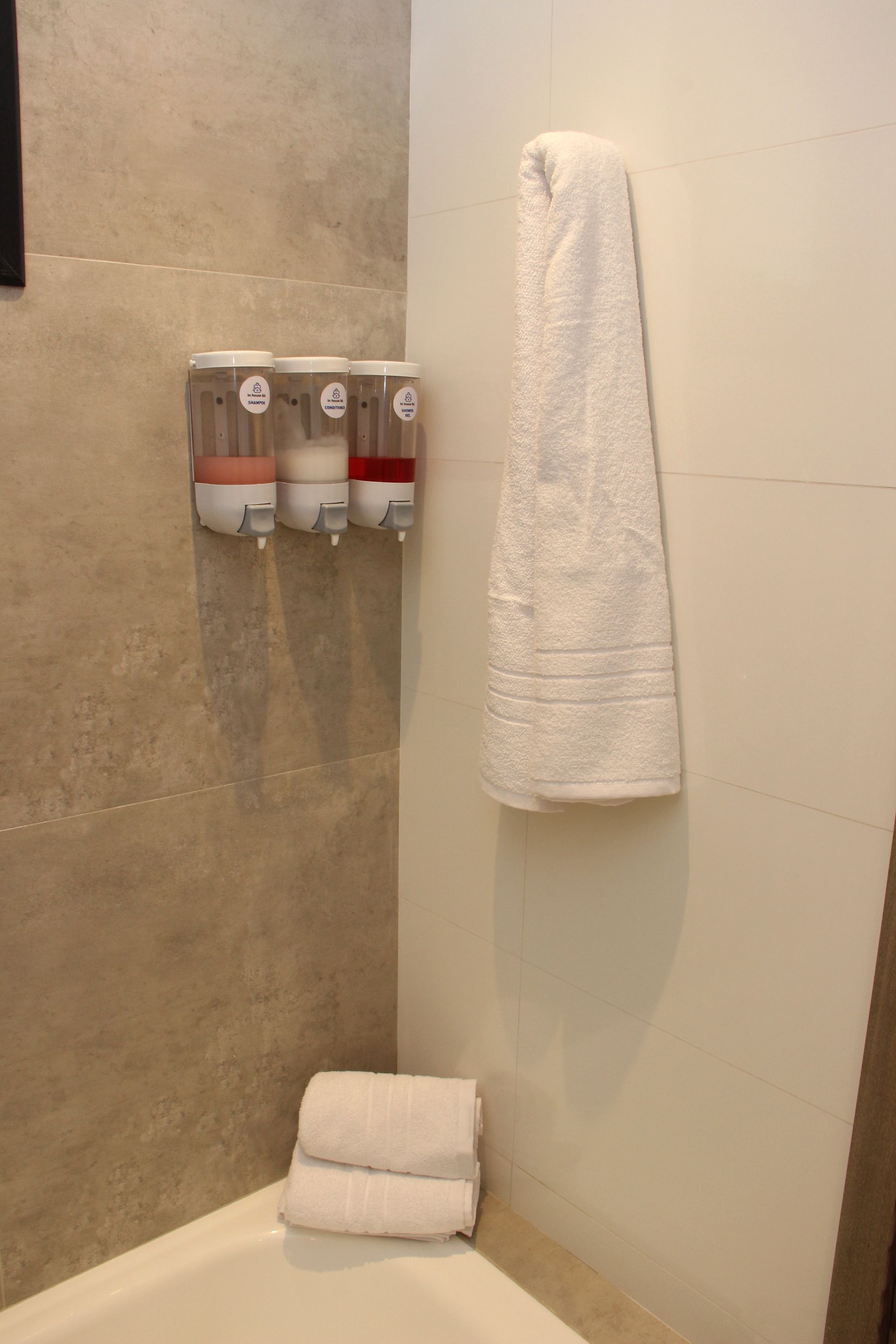 Un baño con tres dispensadores de jabón y una toalla colgada en la pared.