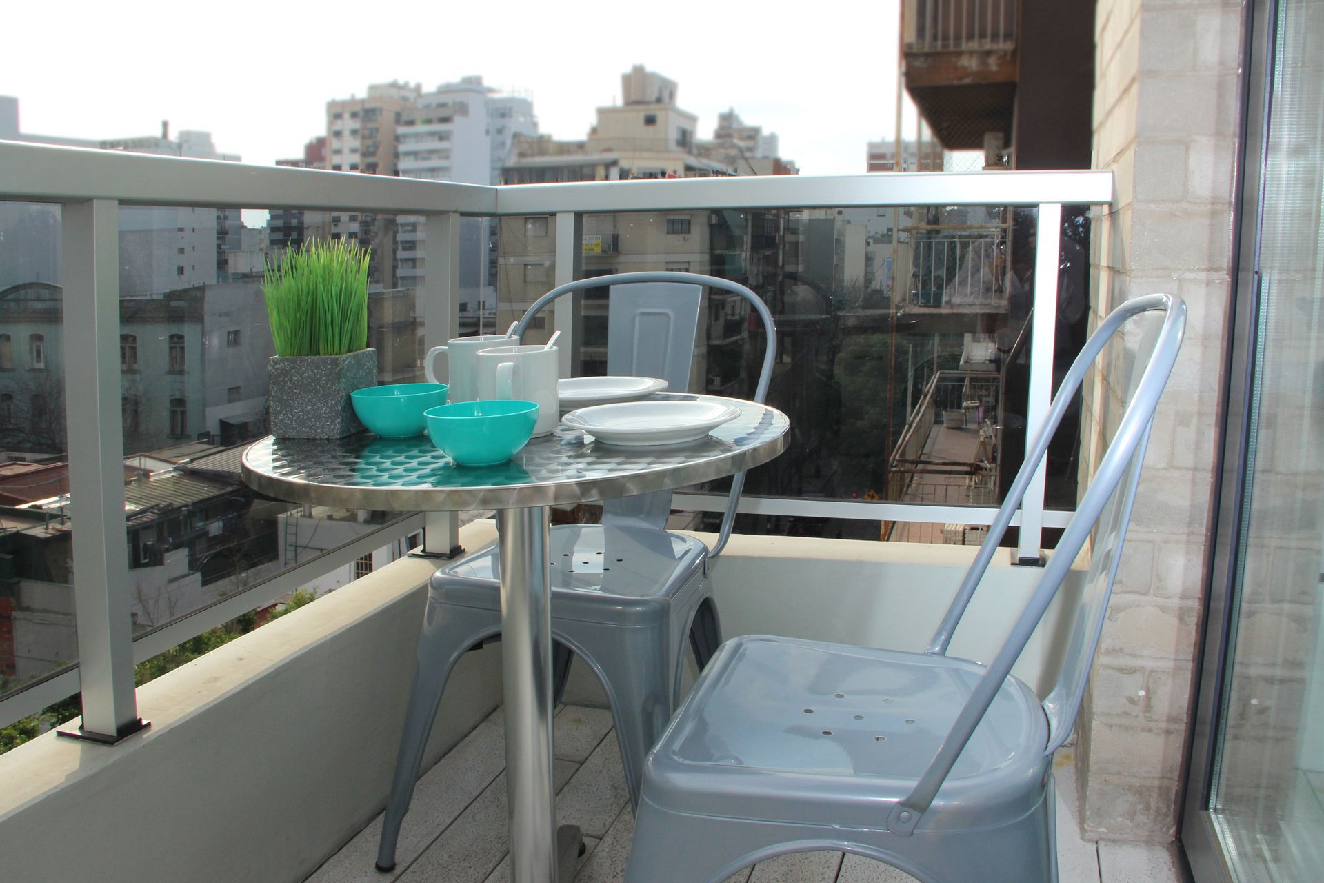 Una pequeña mesa y sillas en un balcón con vista a una ciudad.