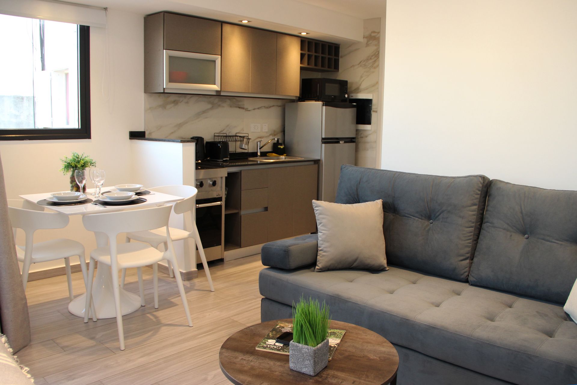 Una sala de estar con sofá, mesa, sillas y una cocina.