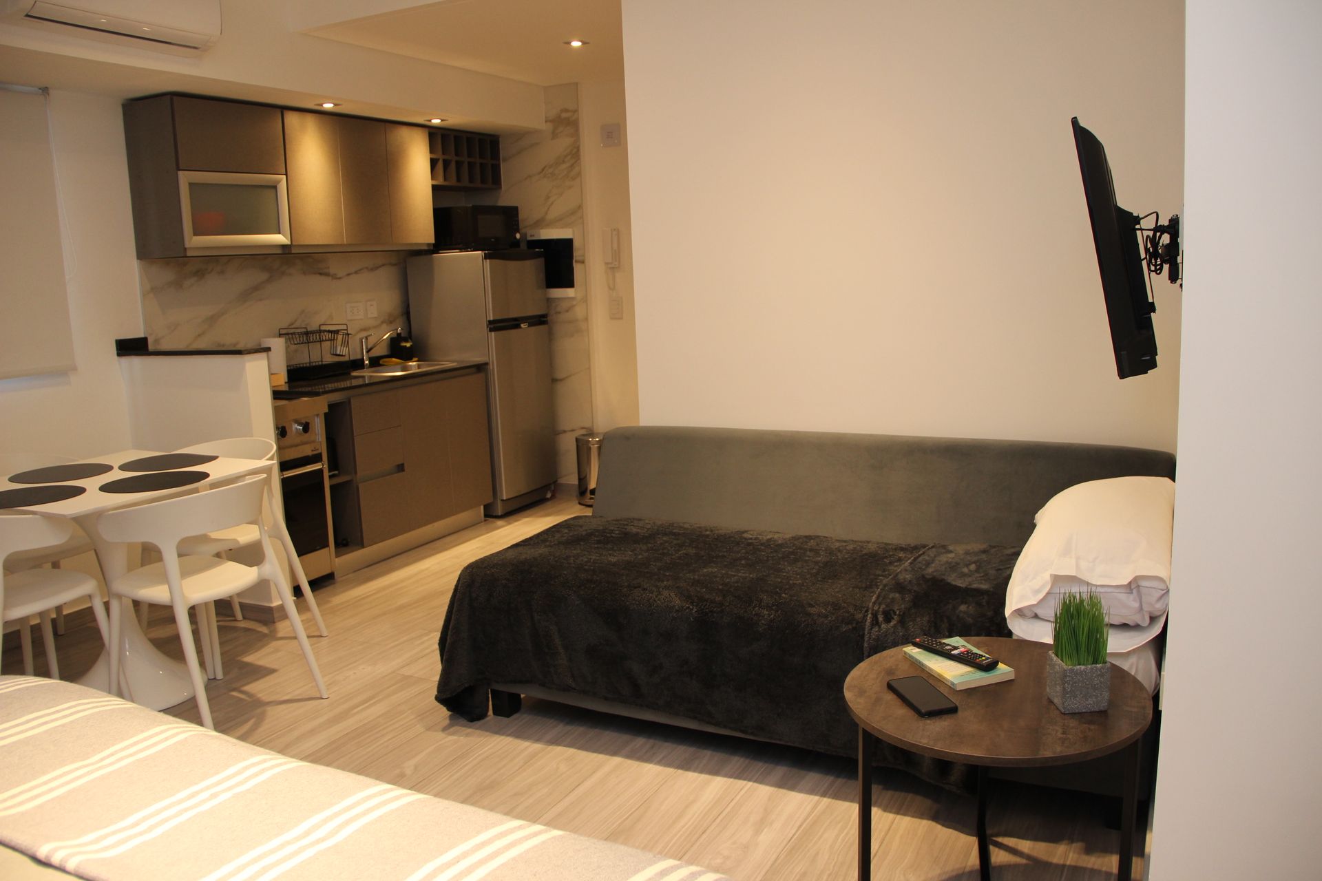 Una sala de estar con un sofá, una mesa, sillas y un televisor montado en la pared.