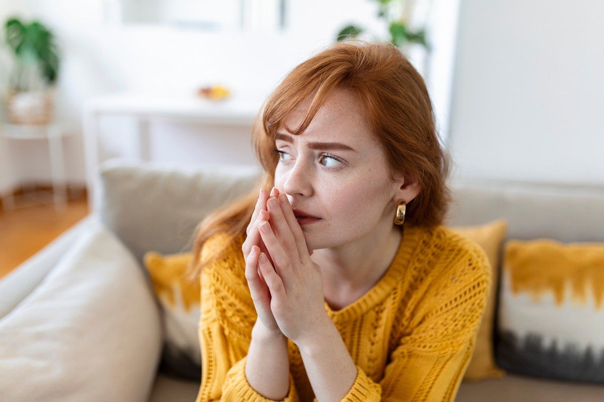 Woman sitting on a couch, looking worried and deep in thought.