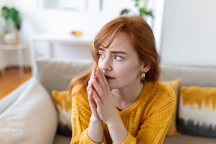 A woman is sitting on a couch with her hands on her face.