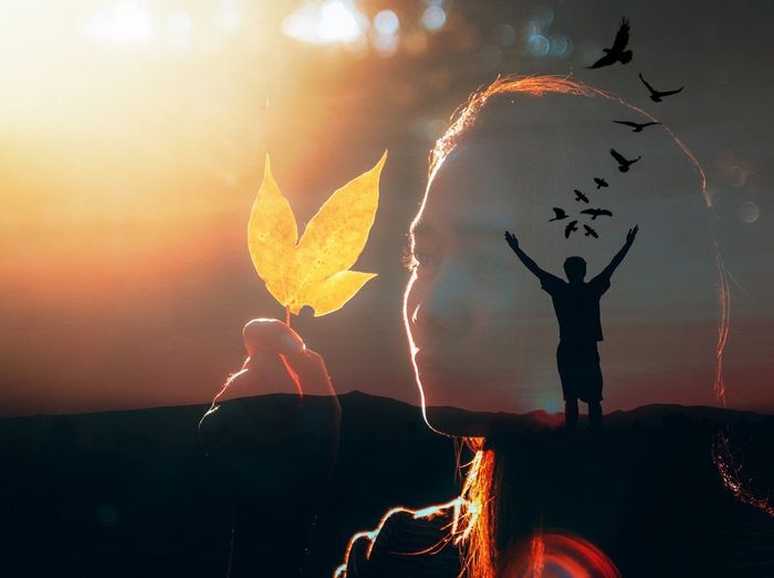 A double exposure of a man holding a leaf and birds flying out of his head.