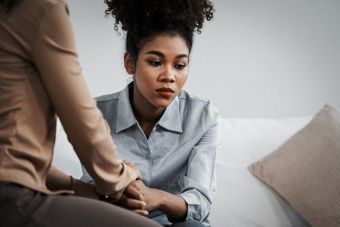 A woman is sitting on a couch talking to another woman.