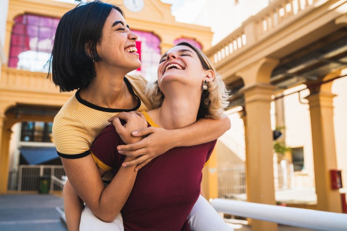 Two women laughing and hugging playfully outdoors.